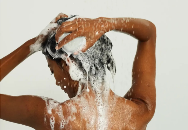 A woman in a shower covered in rich, white soapy lather, holding a Beauty Disrupted bar, emphasizing the high-performance foam and sensory experience of the solid ritual.