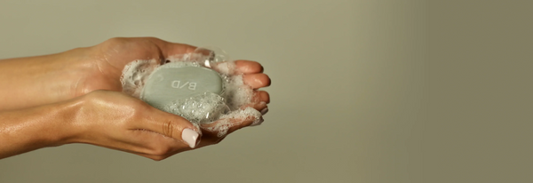 Beauty Disrupted luxury solid shampoo with lather taken in the hands. Plain background.