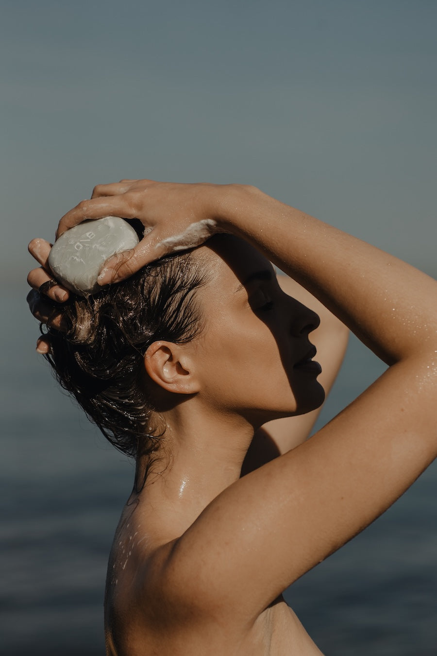Model using a Beauty Disrupted luxury solid shampoo against a blurred natural background